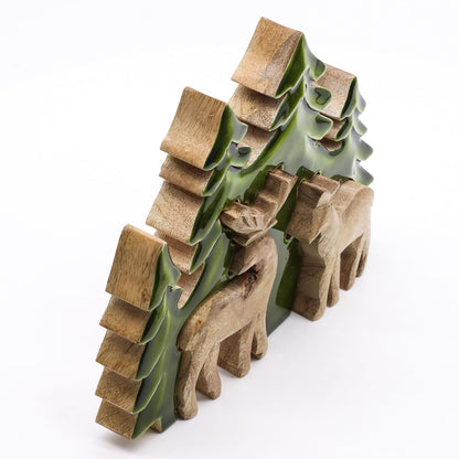 3D mango wood deer in forest decoration with two standing deer, green enamel trees and layered woodland scene on mantel with fairy lights and pine cones