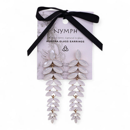 Delicate pearl-white vintage glass long drop earrings swaying gently, catching dawn light against soft white fabric and morning mist