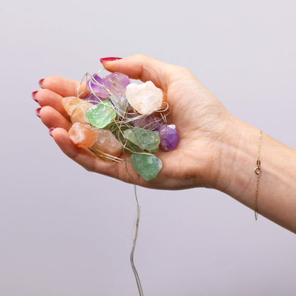 Mixed gemstone fairy lights glowing in glass bowl with amethyst, rose quartz, jade and clear quartz crystals sparkling on boho bedroom shelf