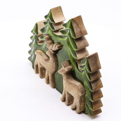 3D mango wood deer in forest decoration with two standing deer, green enamel trees and layered woodland scene on mantel with fairy lights and pine cones