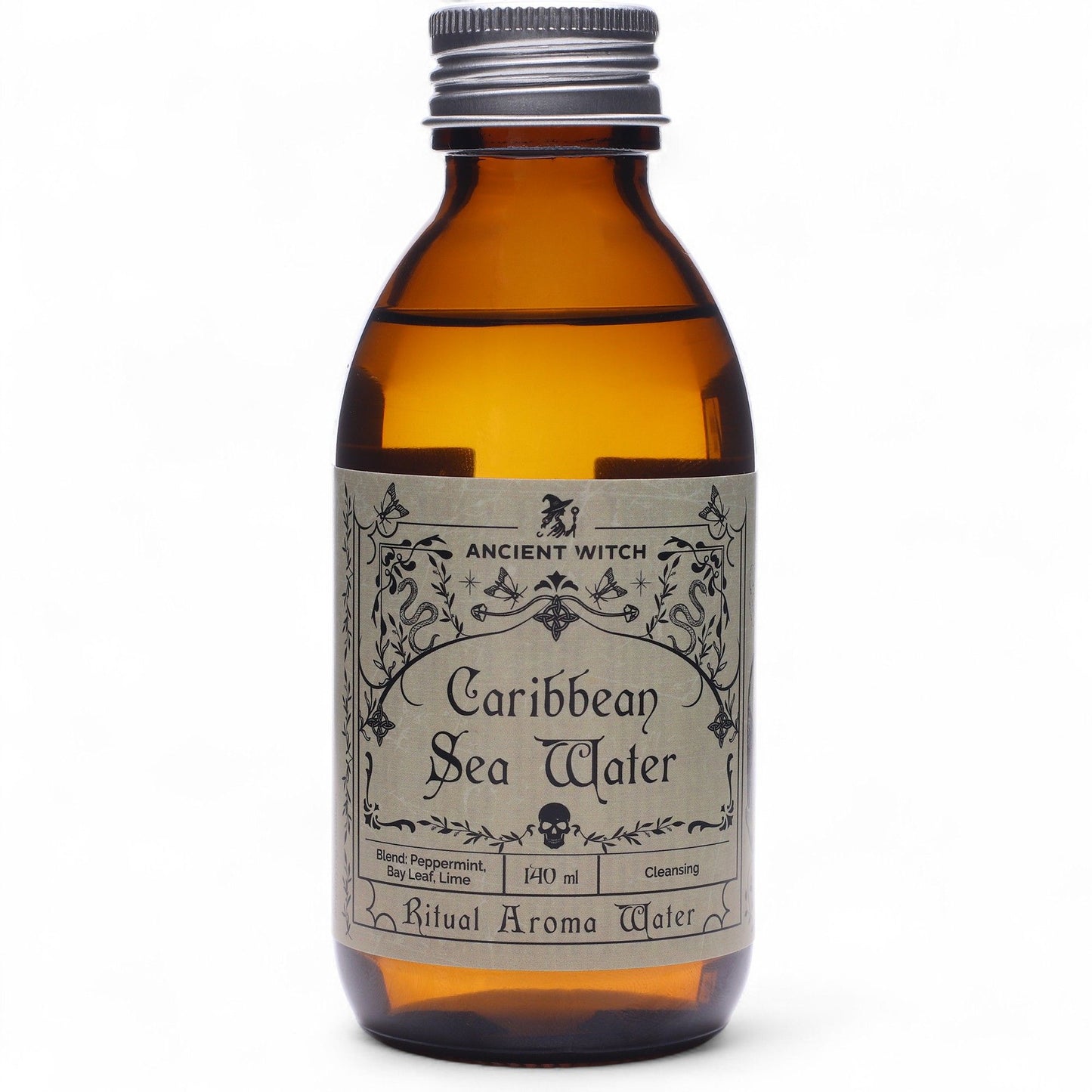 140ml amber bottle of Caribbean Sea Ritual Water with pirate-map label, surrounded by fresh limes, bay leaves, peppermint sprigs and ocean treasures