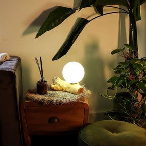 Glowing spherical lamp on a wooden side table with plants and a couch