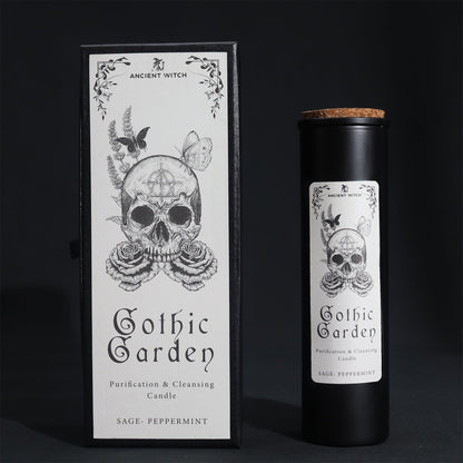 Black glass Gothic Garden candle burning with green flame, skull & roses label, surrounded by fresh sage nand peppermint leaves