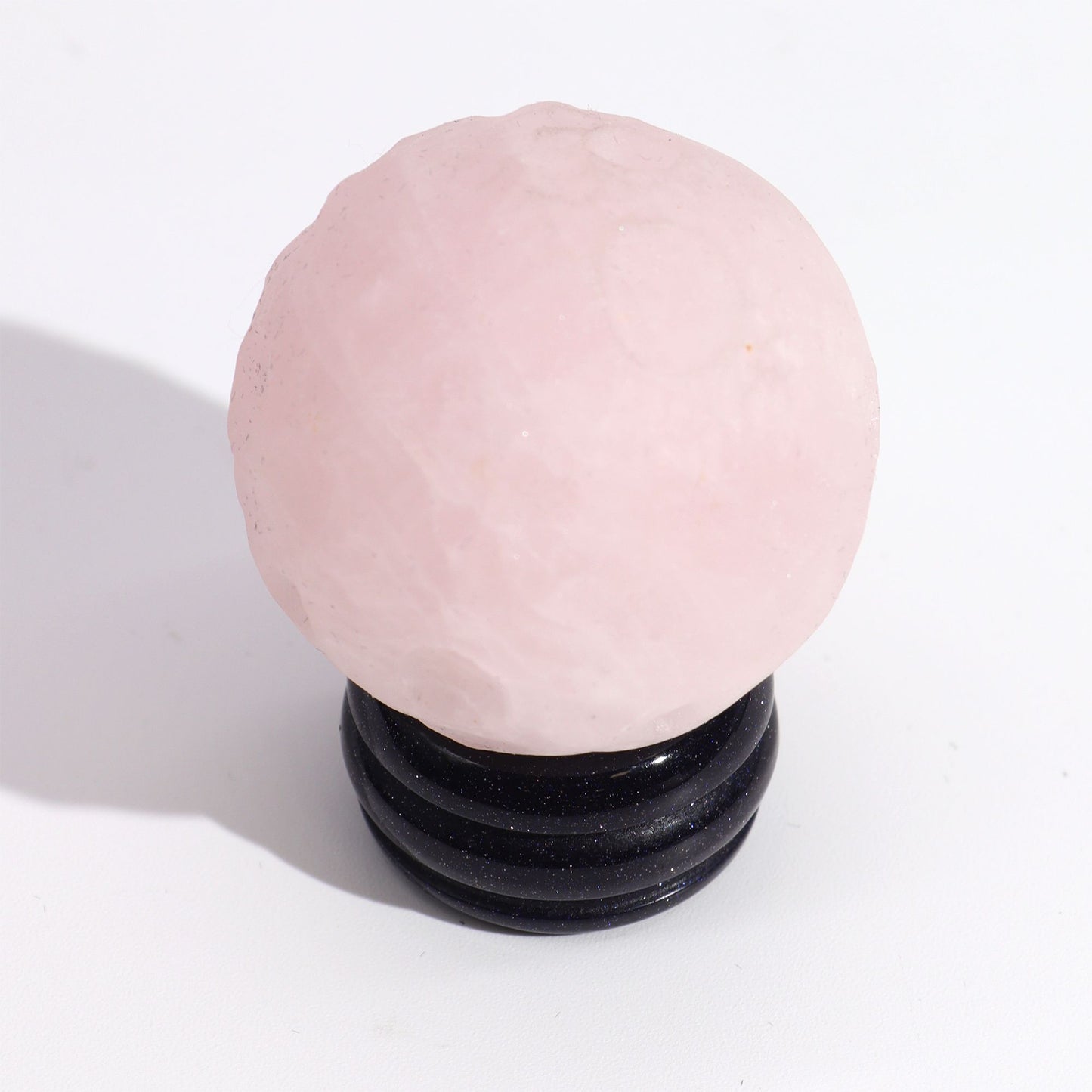 Soft pink 40mm Rose Quartz Venus sphere glowing on glittering goldstone ring stand, surrounded by rose petals and candles in romantic setting