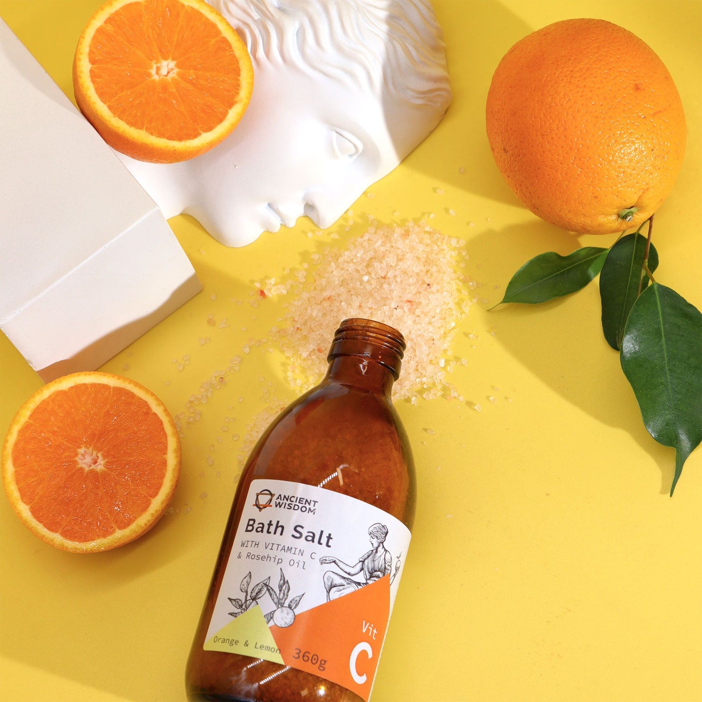 Bottle of bath salt with oranges and a white towel on a yellow background