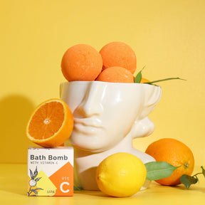 Bath bomb with vitamin C packaging on a yellow background with oranges and lemons.