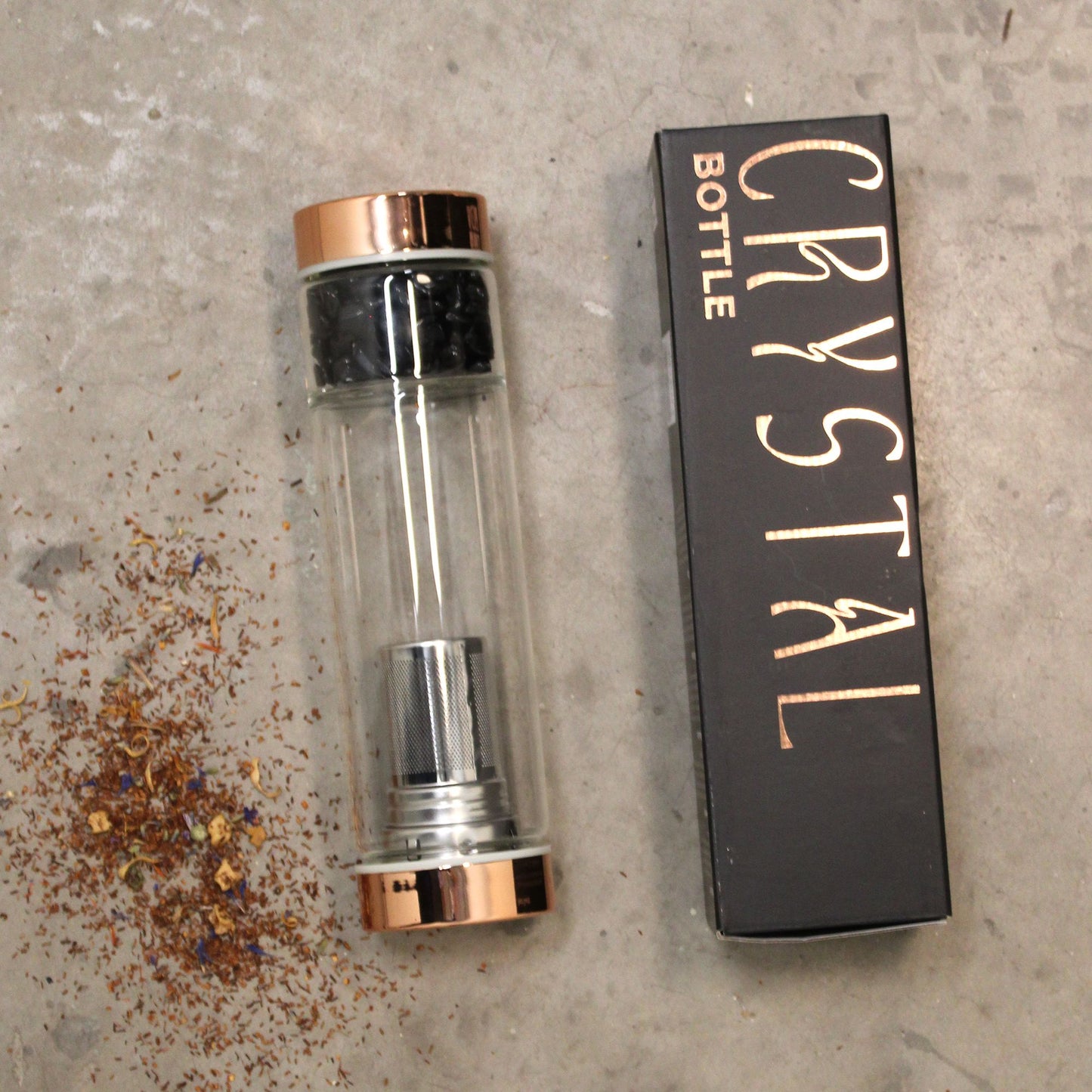 Rose gold amethyst crystal tea infuser bottle with removable bottom chamber full of purple amethyst chips, neoprene sleeve, loose leaf tea and steaming brew