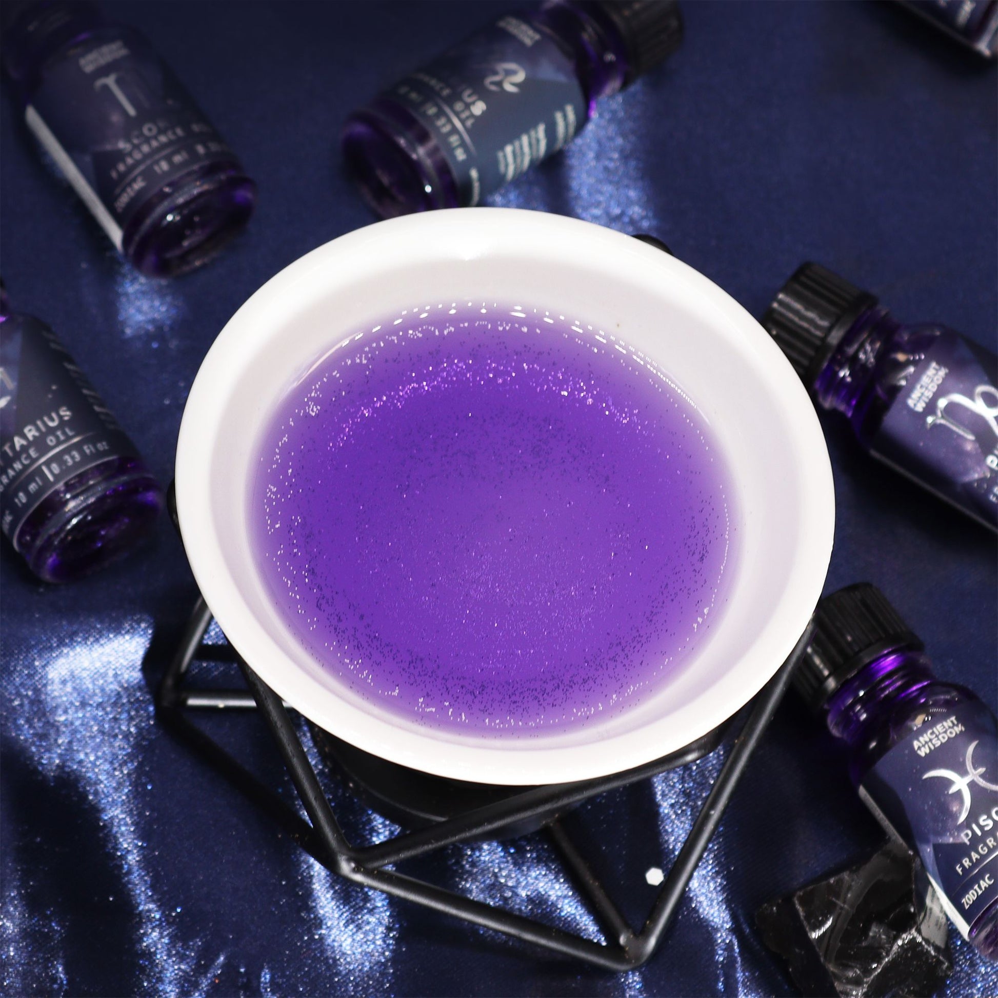 Purple liquid in a white bowl surrounded by dark bottles on a reflective surface