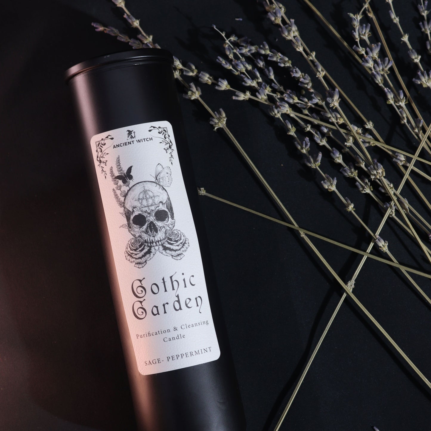 Black glass Gothic Garden candle burning with green flame, skull & roses label, surrounded by fresh sage nand peppermint leaves