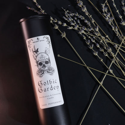 Black glass Gothic Garden candle burning with green flame, skull & roses label, surrounded by fresh sage nand peppermint leaves