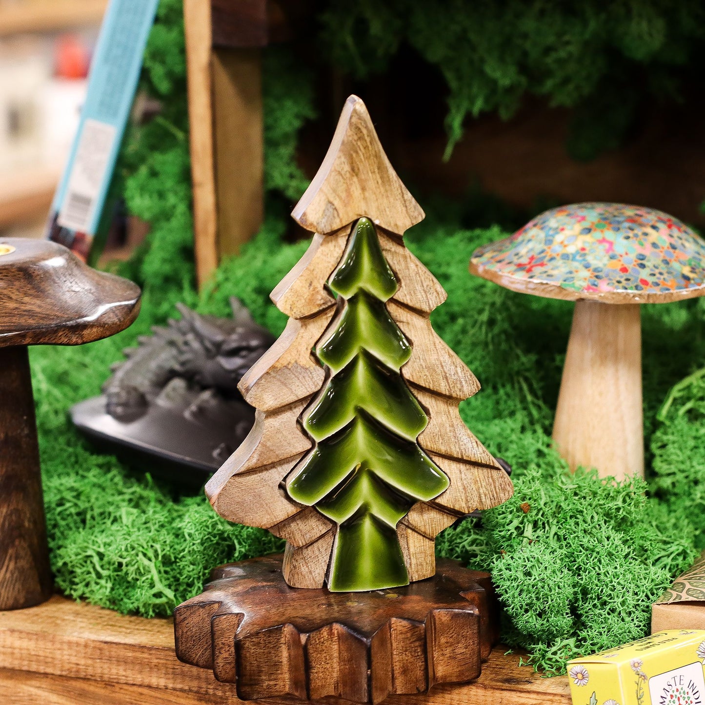 Wooden and ceramic tree figurine on a miniature landscape with a mushroom and other elements.