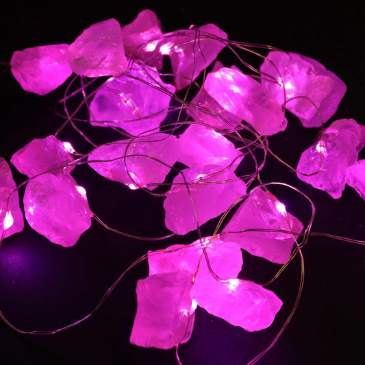 Rose quartz crystal fairy lights glowing soft pink in glass vase on bedroom dresser with roses, candles and love crystals in romantic setting