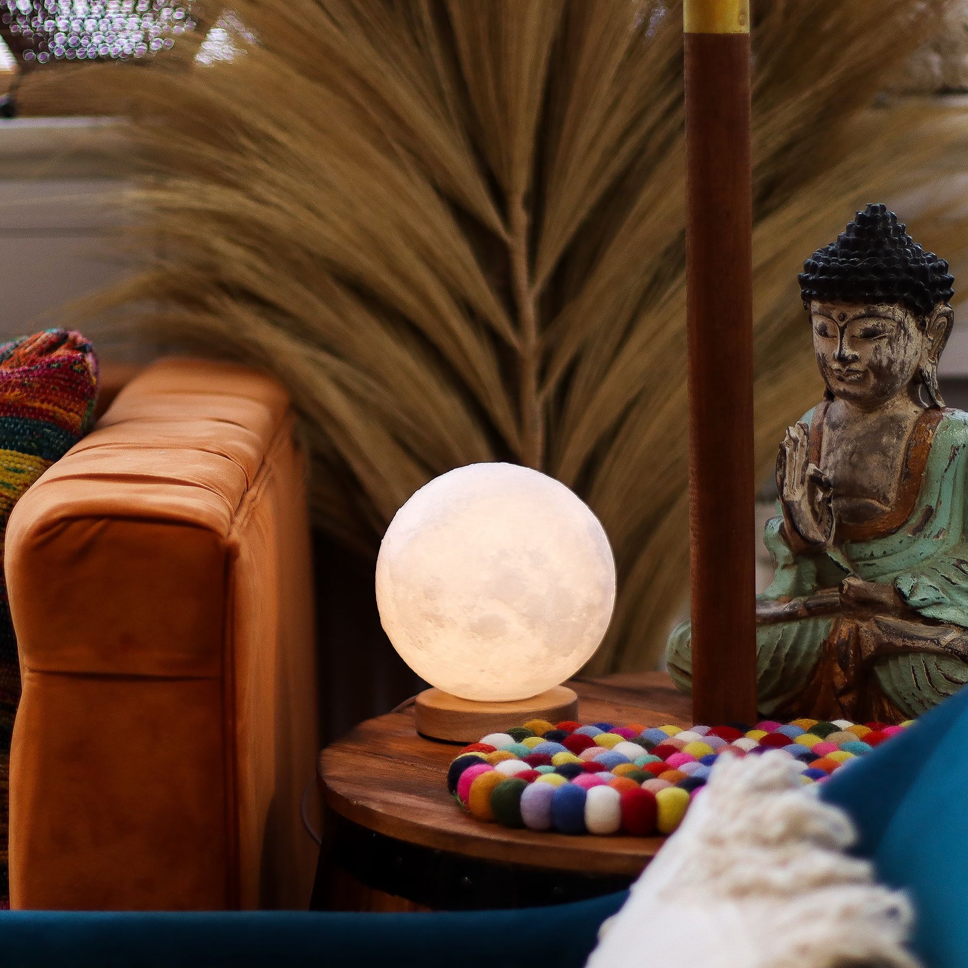 Decorative Moon New Wave USB lamp with textured honeycomb surface and crescent moon-inspired shape, warm glow on 3rd brightness setting, placed on a wooden base on a small table with a statue and colorful items in a cozy room.