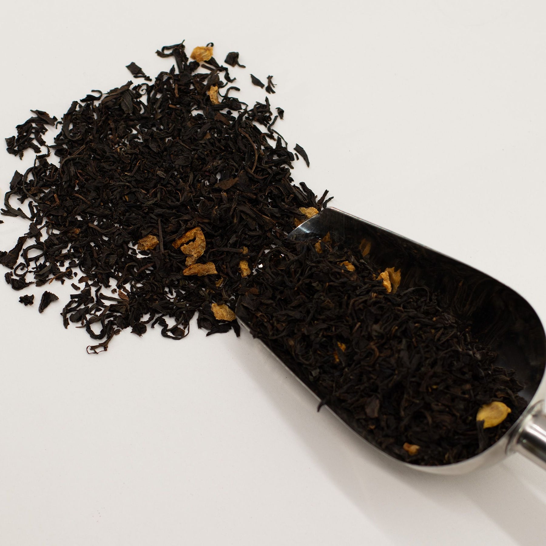 Black tea leaves in a metal scoop on a white background