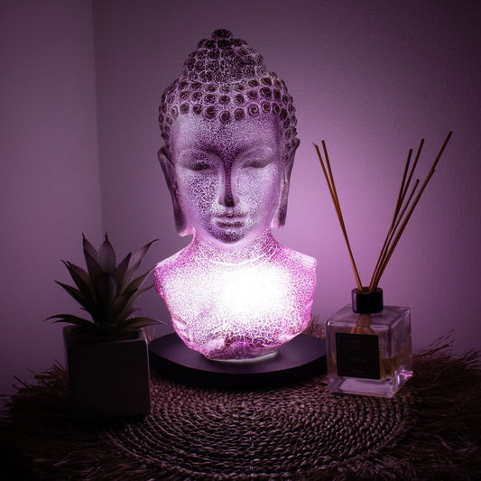 Buddha Bust Lamp with crackle textured surface on modern oval stand, emitting soft warm ambient glow in a calm living space with subtle lighting
