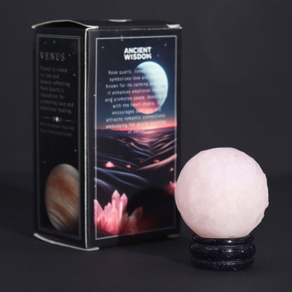 Soft pink 40mm Rose Quartz Venus sphere glowing on glittering goldstone ring stand, surrounded by rose petals and candles in romantic setting