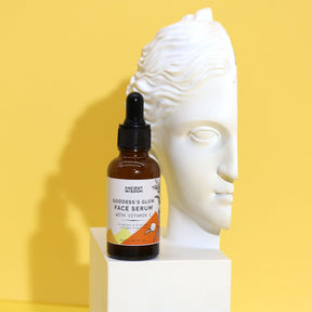 Face serum bottle with dropper on a white pedestal against a yellow background