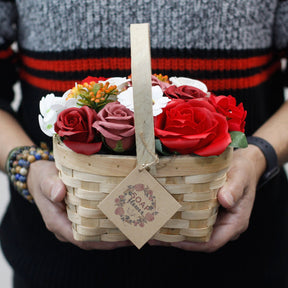 Person holding a basket of soap flowers with a visible brand tag.
