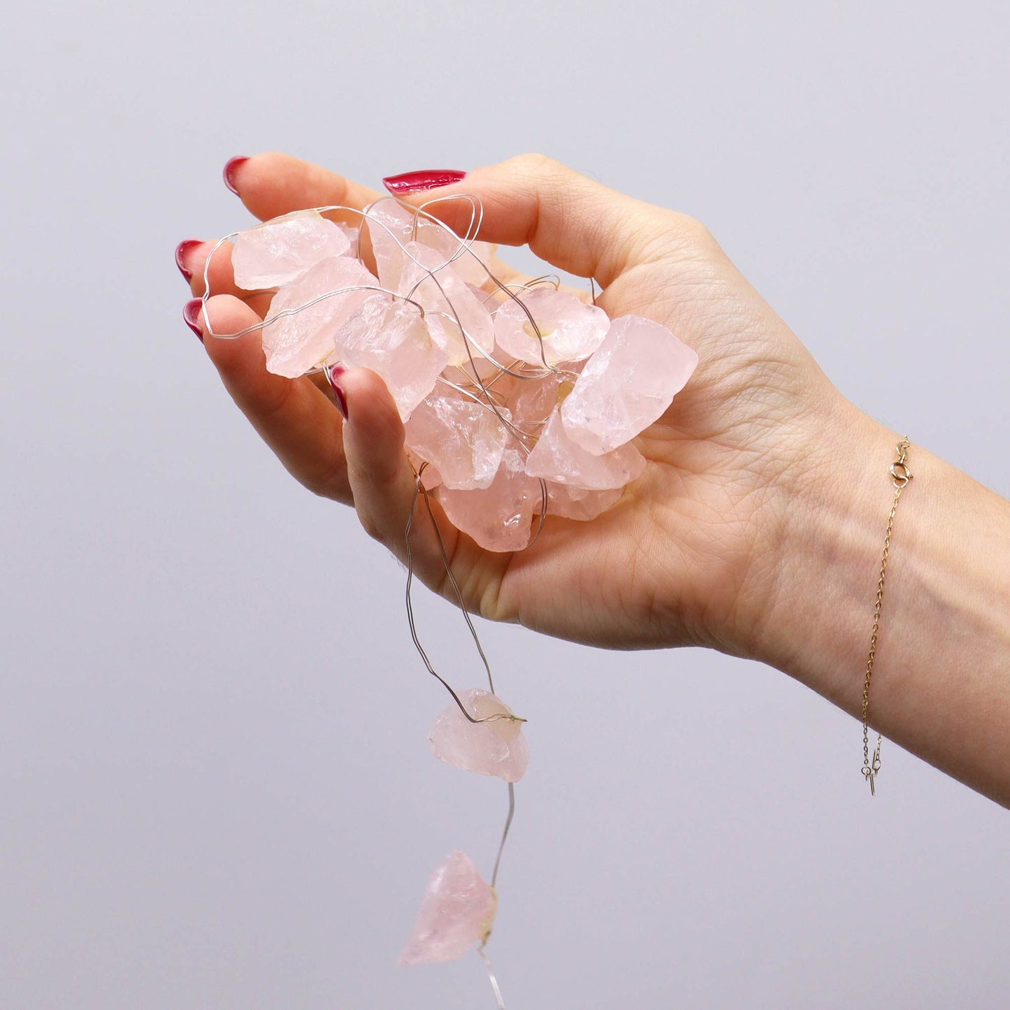 Rose quartz crystal fairy lights glowing soft pink in glass vase on bedroom dresser with roses, candles and love crystals in romantic setting