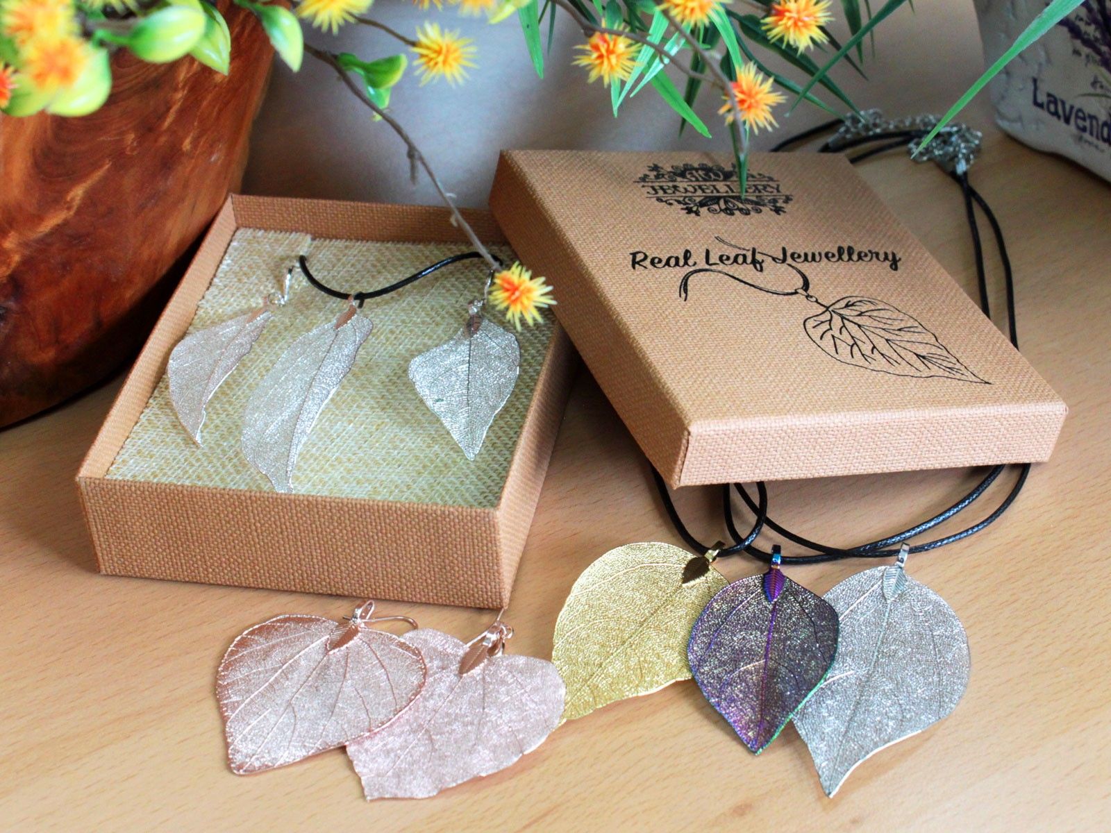 Real leaf jewelry displayed on a wooden surface with branded packaging.
