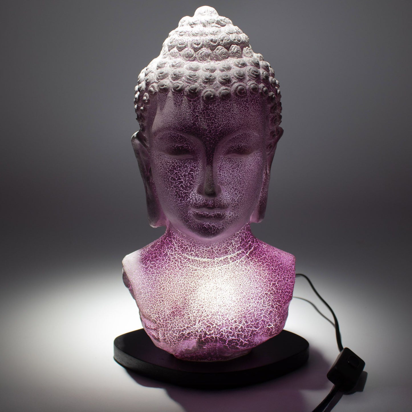 Buddha Bust Lamp with crackle textured surface on modern oval stand, emitting soft warm ambient glow in a calm living space with subtle lighting