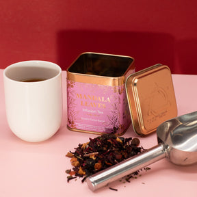 Tea canister with a scoop of tea leaves and a white cup on a pink surface with a red background