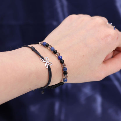 Hand wearing a bracelet with a butterfly charm against a dark background