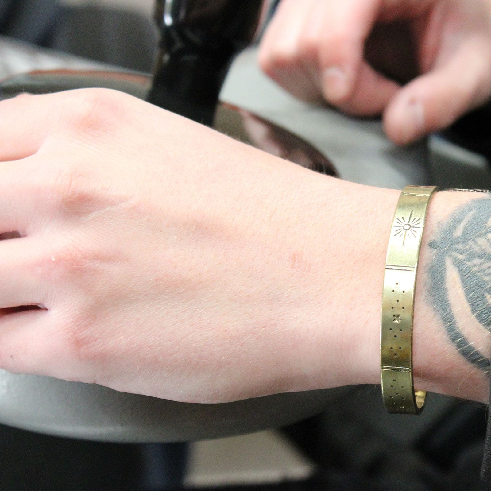 Hand-hammered brass galaxy cuff from Nepal with secret inner mantra (Dream Big, Reach For The Stars & more). Stars & Earth design outside. Fair-trade, adjustable on a wrist with a blurred background