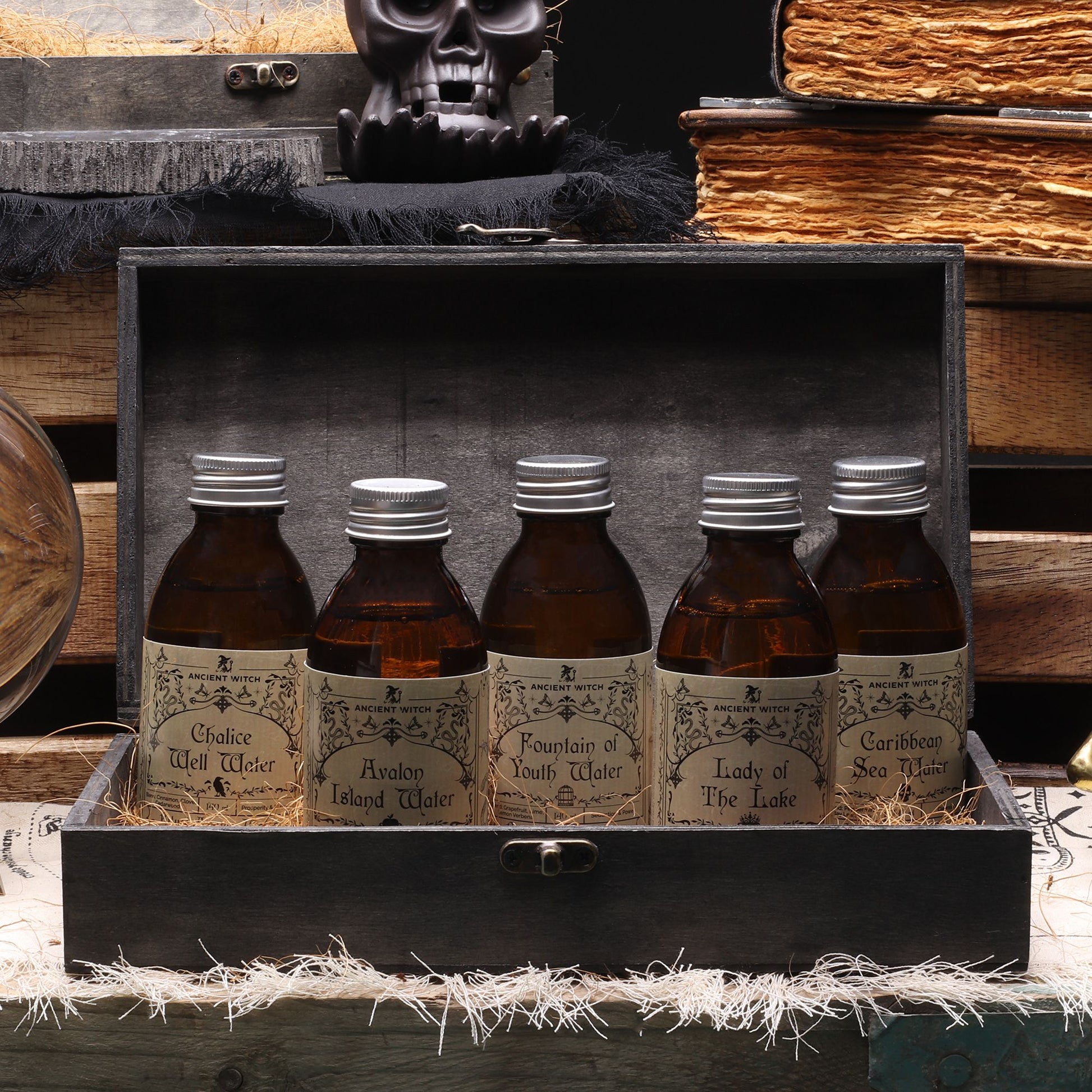 Five bottles of 'Water' in a wooden box with a skull and books in the background