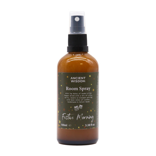 100ml Festive Morning room spray in matte amber bottle with gold sprayer, surrounded by cinnamon sticks, jasmine flowers and velvet ribbon on dark wooden table