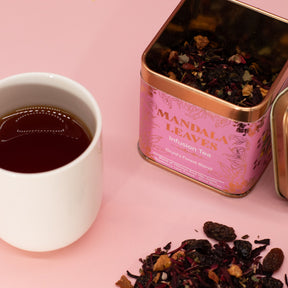 Tea cup with mandala leaves tea canister and scattered tea leaves on a pink background