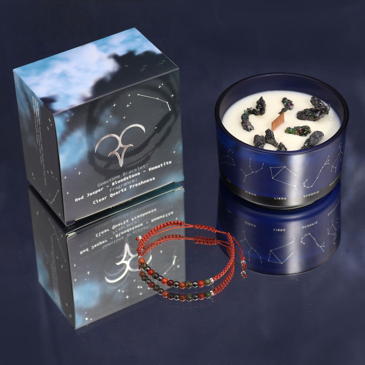 Candle in a blue container with a box and bracelet on a reflective surface