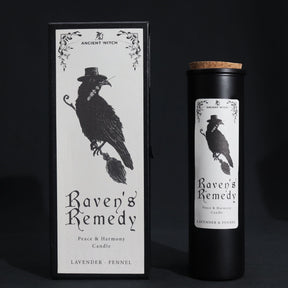Black matte glass Raven’s Remedy candle burning with purple flame, surrounded by raven feathers, dried lavender, fennel seeds and a spell card on dark velvet