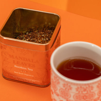 Mandala Leaves Rooibos Tea tin with a cup of tea on an orange background