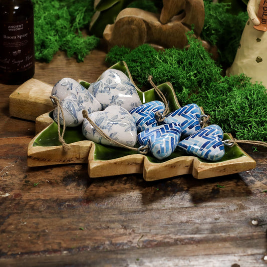 Decorative heart-shaped stones with blue and white patterns on a wooden tray with green moss.