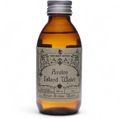 140ml amber bottle of Avalon Island ritual water with misty isle & nine priestesses label, surrounded by fresh lavender, roses and glowing candles