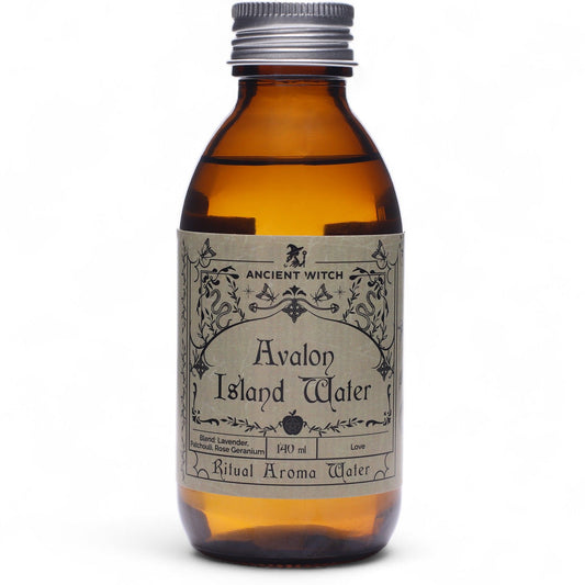 140ml amber bottle of Avalon Island ritual water with misty isle & nine priestesses label, surrounded by fresh lavender, roses and glowing candles