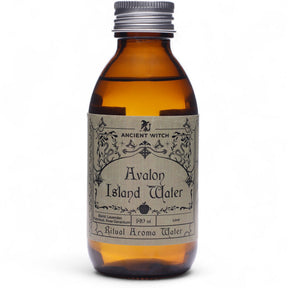 140ml amber bottle of Avalon Island ritual water with misty isle & nine priestesses label, surrounded by fresh lavender, roses and glowing candles