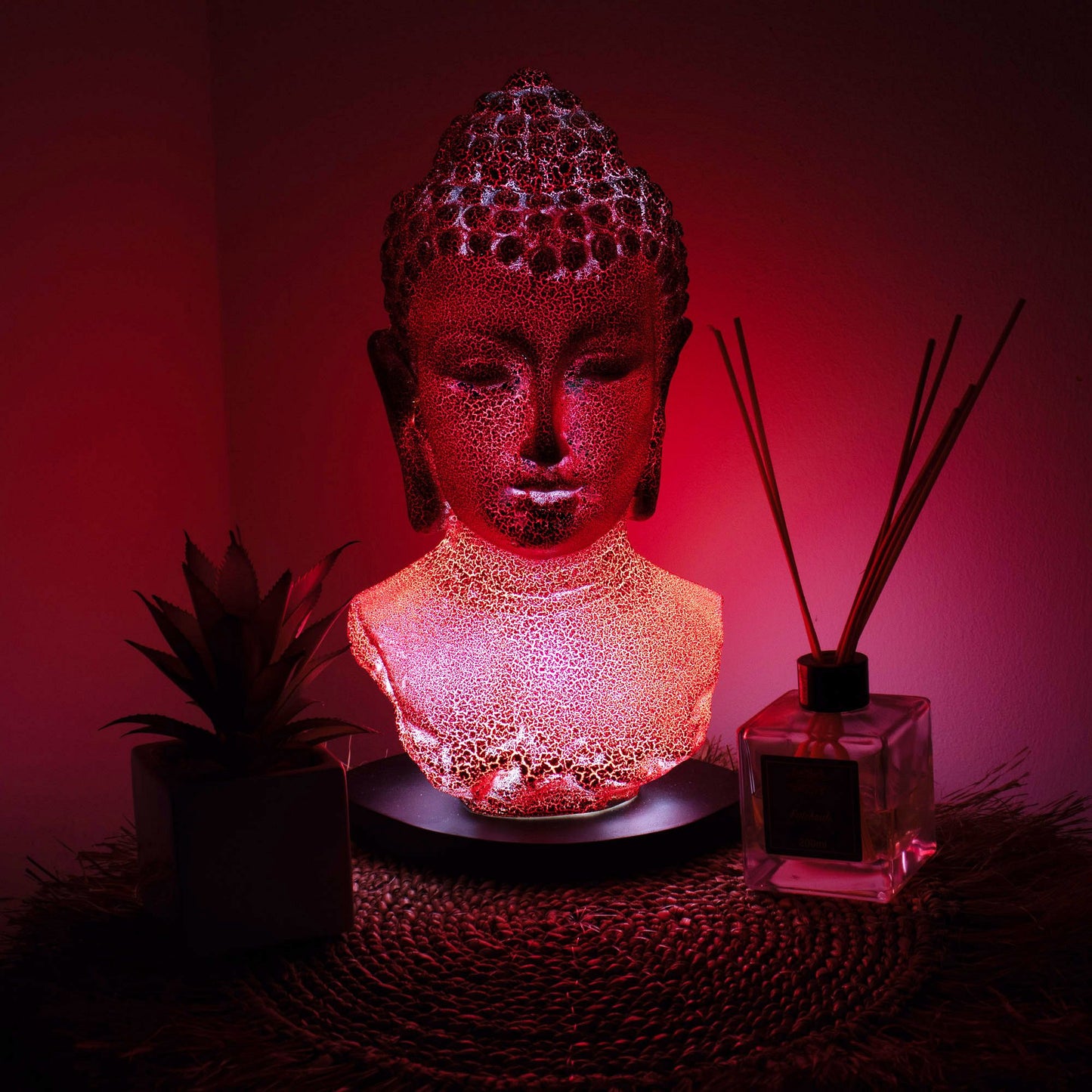 Buddha Bust Lamp with crackle textured surface on modern oval stand, emitting soft warm ambient glow in a calm living space with subtle lighting