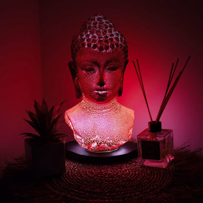 Buddha Bust Lamp with crackle textured surface on modern oval stand, emitting soft warm ambient glow in a calm living space with subtle lighting
