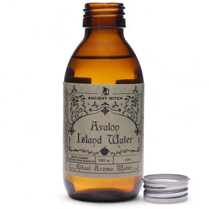 140ml amber bottle of Avalon Island ritual water with misty isle & nine priestesses label, surrounded by fresh lavender, roses and glowing candles