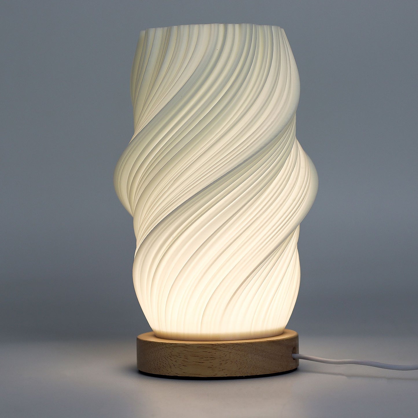 Close-up of lamp’s textured honeycomb pattern and soft diffused light, showing elegant cloud-like twisted shape and wooden base detail