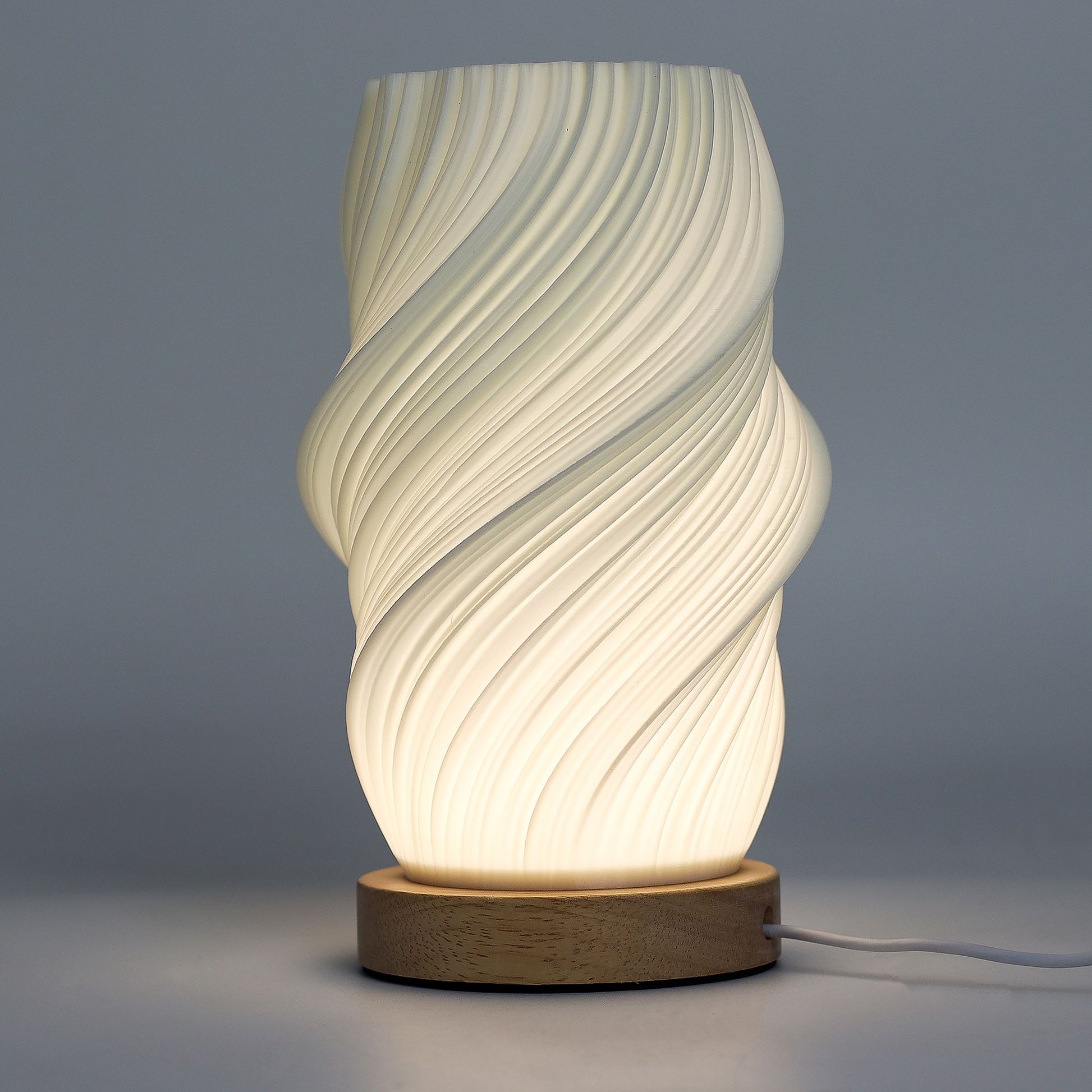 Close-up of lamp’s textured honeycomb pattern and soft diffused light, showing elegant cloud-like twisted shape and wooden base detail