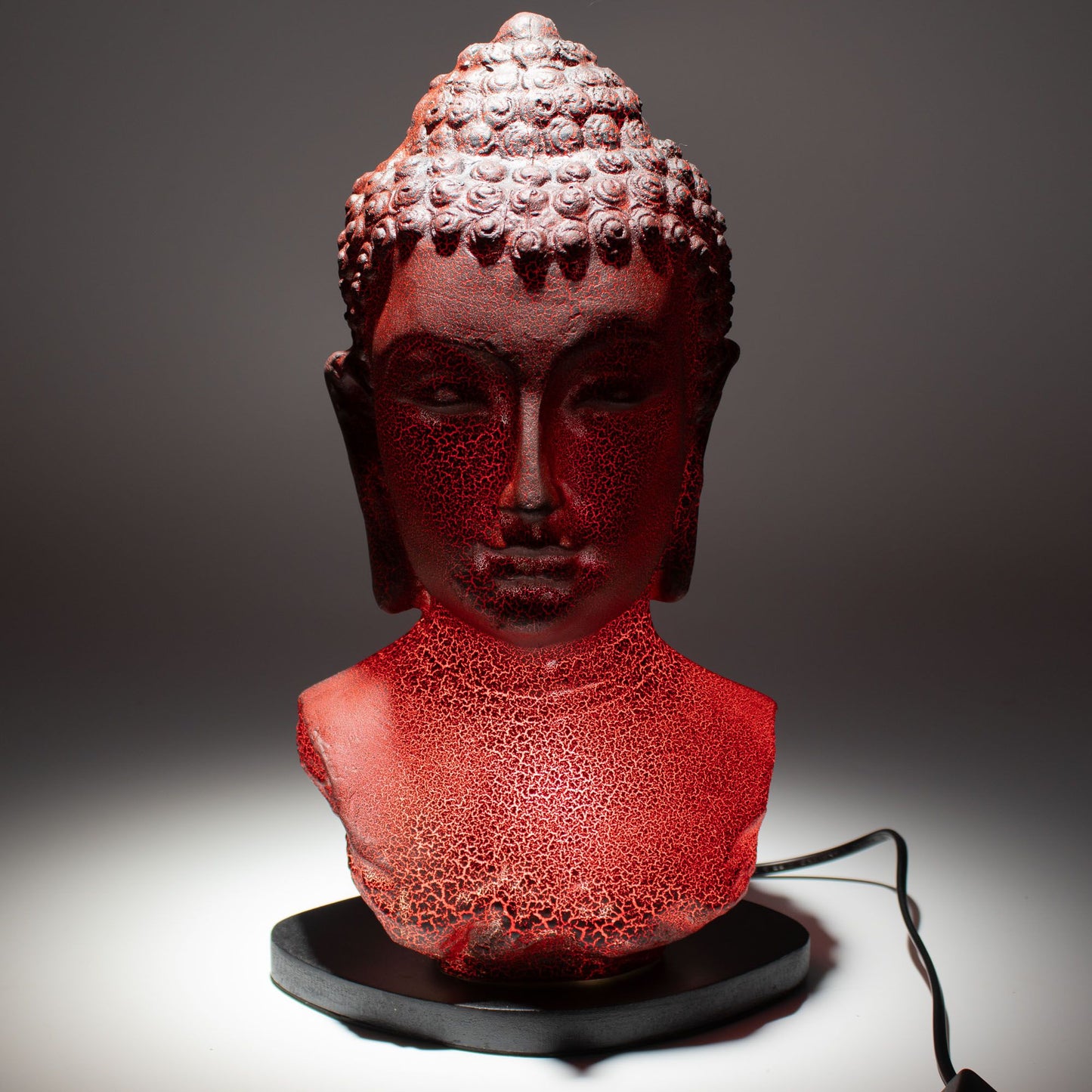 Buddha Bust Lamp with crackle textured surface on modern oval stand, emitting soft warm ambient glow in a calm living space with subtle lighting