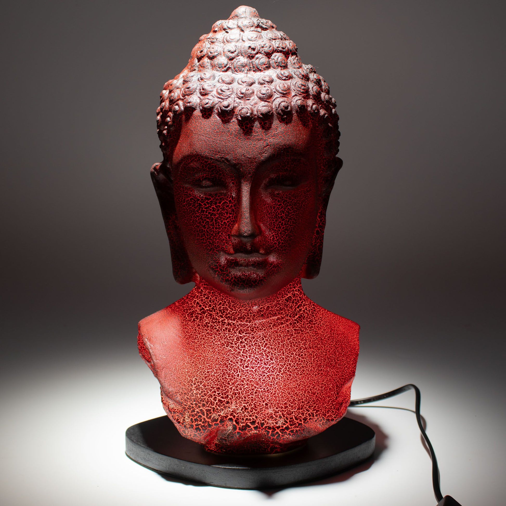 Buddha Bust Lamp with crackle textured surface on modern oval stand, emitting soft warm ambient glow in a calm living space with subtle lighting