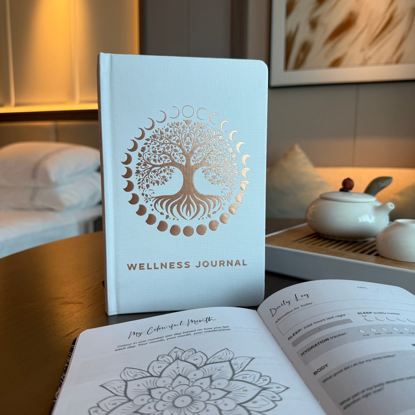 Elegant white wellness journal with rose gold foil Tree of Life, open to mood tracker and affirmation pages, styled with crystals, rose quartz and candle
