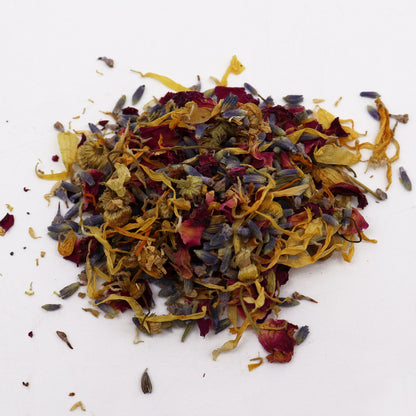 250g jar of dried lavender buds, rose petals, chamomile & calendula flowers spilling onto white marble with steaming bowl in soft spa setting