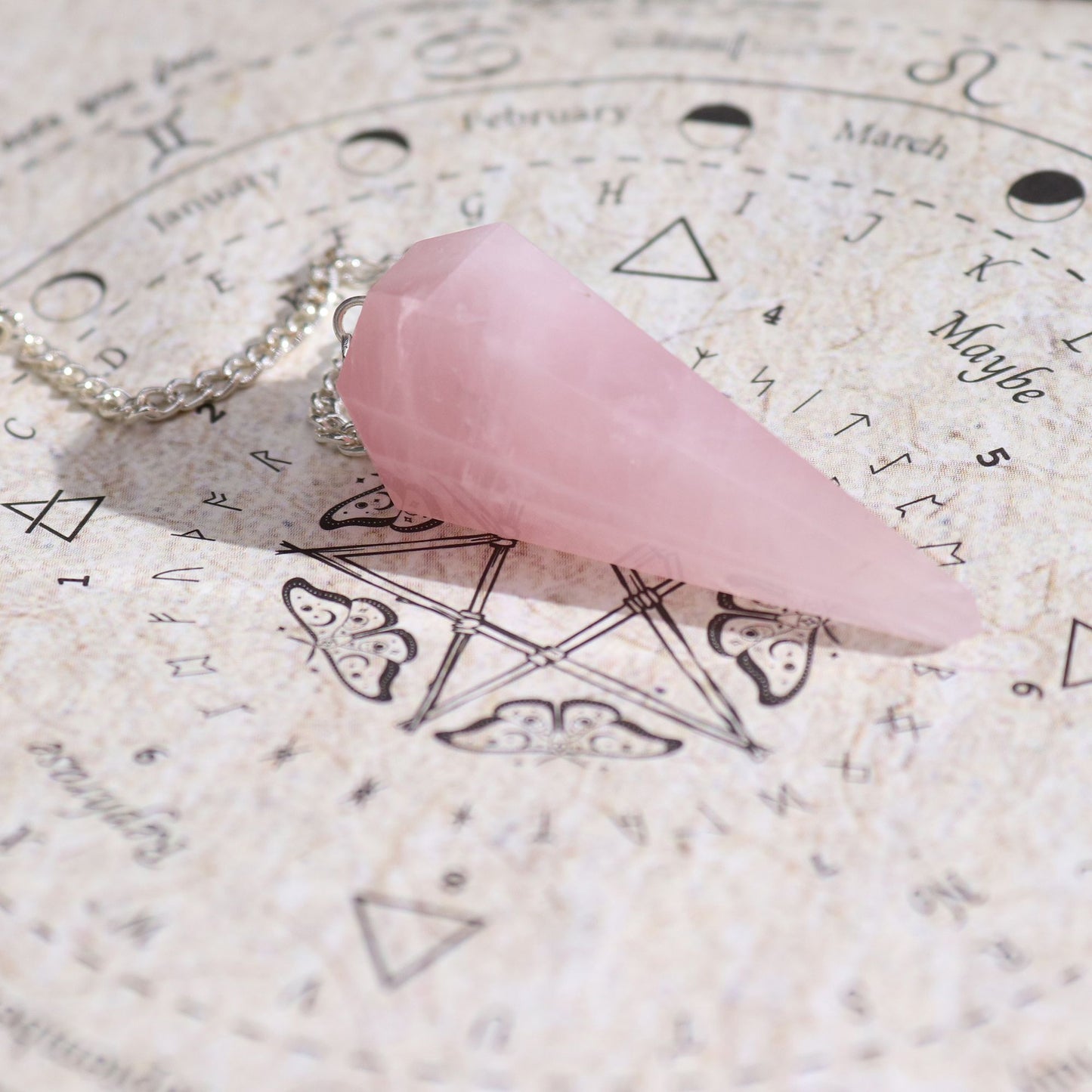 Pink crystal pendulum on an astrological chart