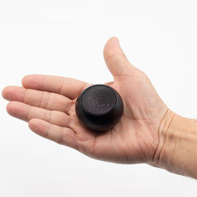 Palm-sized Beyond Size mini Bluetooth speaker in sleek modern design held in hand, showing compact scale, one-button control and subtle LED indicator