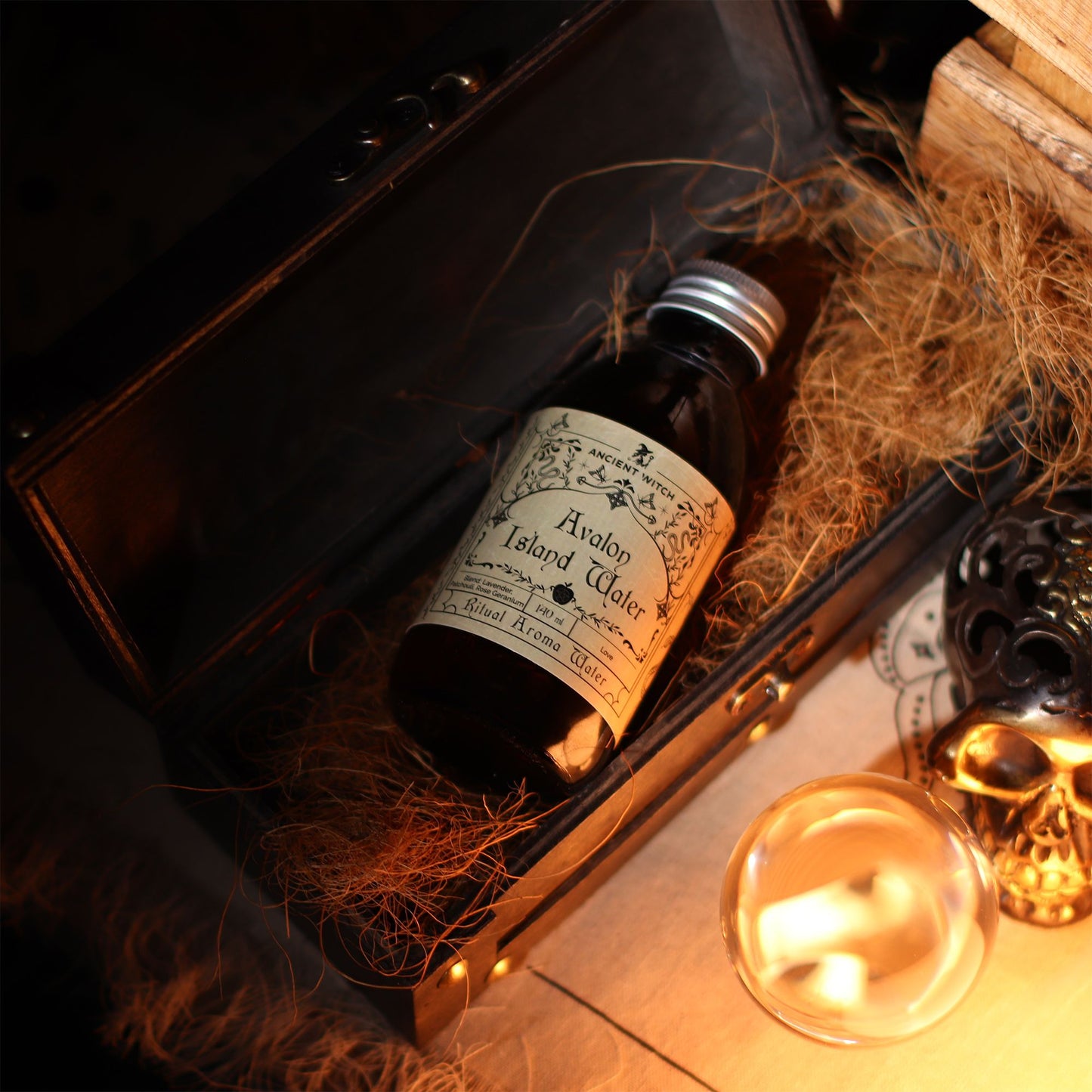 140ml amber bottle of Avalon Island ritual water with misty isle & nine priestesses label, surrounded by fresh lavender, roses and glowing candles